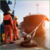 Coface: United States Country Risk Focus. The photo shows two men in high viz protective equipment standing by a ship in a harbour.